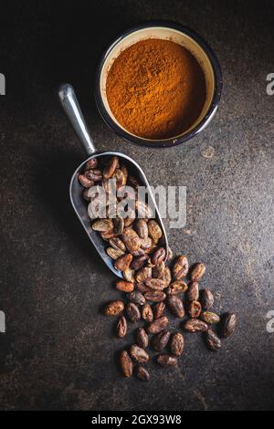 Poudre de cacao et fèves de cacao en cuillère sur table noire. Vue de dessus. Banque D'Images