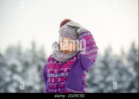 une petite fille en hiver vêtu de pourpre marche à travers une forêt enneigée. Banque D'Images