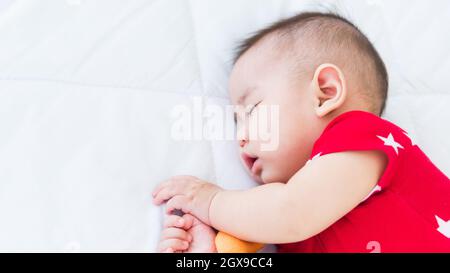 Portrait de beau nouveau-né asiatique petit bébé dormant sur un lit blanc à la maison, bébé heureux porte une chemise rouge relaxant oreiller dans la chambre, famille Mornin Banque D'Images