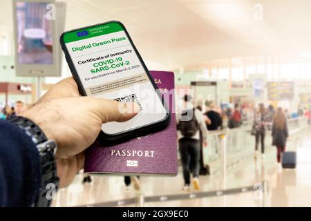 Main d'homme tenant un téléphone avec le certificat de vaccination de l'Union européenne à l'écran et un passeport traditionnel à l'intérieur d'un aéroport. Immunité de Co Banque D'Images