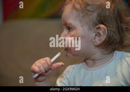 Petite fille mignonne mangeant son désert de chocolat après le dîner avec une cuillère et faire un sale visage sale Banque D'Images