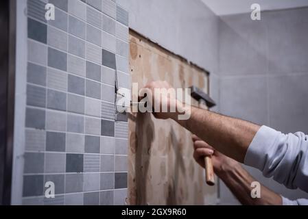 le travailleur professionnel enlève démolir les vieux tuiles dans une salle de bains avec marteau et burin Banque D'Images