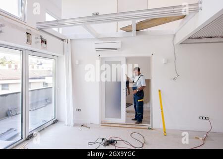 des charpentiers de travailleurs pour hommes installent une porte intérieure en verre avec un cadre en bois dans un nouvel appartement de luxe Banque D'Images