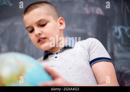 Happy cute boy apprentissage du monde en utilisant globe de terre alors qu'il se tenait devant le tableau noir Banque D'Images