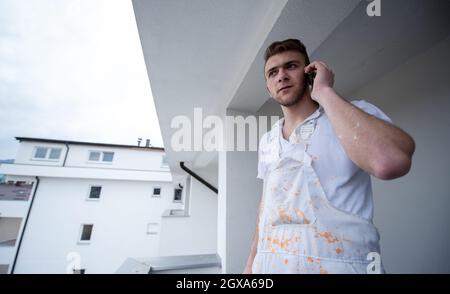 Peintre passer des appels téléphoniques en se tenant sur le balcon pendant la pause de travail Décorateur Utilisant le téléphone mobile debout À L'Extérieur Banque D'Images