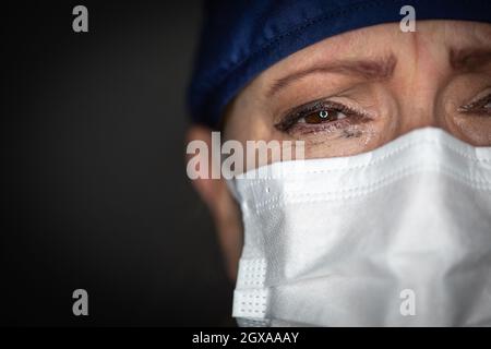 Un médecin ou une infirmière féminine stressée portant un masque facial médical sur fond sombre. Banque D'Images