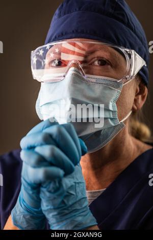 Drapeau américain réfléchissant sur la prière en détresse des travailleuses médicales portant un masque facial de protection et des lunettes de protection. Banque D'Images