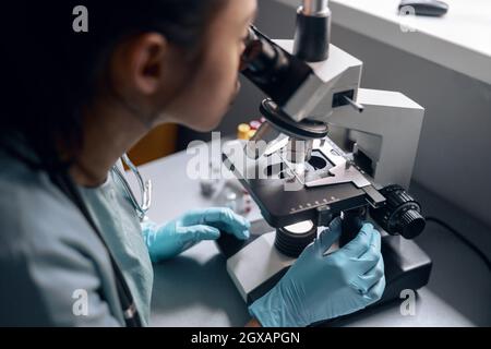 Un jeune travailleur travaille avec un microscope pour la recherche de matériel à la table en laboratoire Banque D'Images