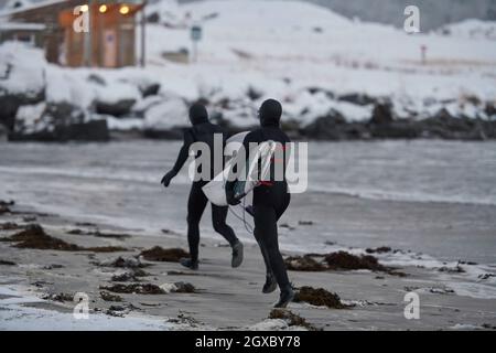 D'authentiques surfeurs arctiques locaux qui s'exécutent sur une plage enneigée après avoir surfé sur la mer norvégienne. Fond de montagne enneigé en hiver. Norwegian Lofoten Banque D'Images