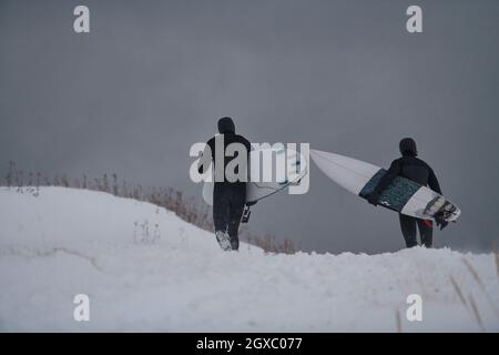 D'authentiques surfeurs arctiques locaux qui s'exécutent sur une plage enneigée après avoir surfé sur la mer norvégienne. Fond de montagne enneigé en hiver. Norwegian Lofoten Banque D'Images