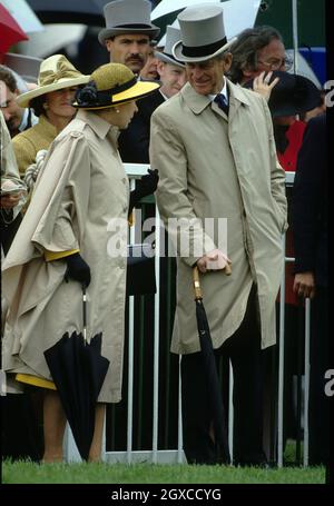La reine Elizabeth ll et le prince Philip, duc d'Édimbourg, portent des manteaux de pluie au Derby. Banque D'Images