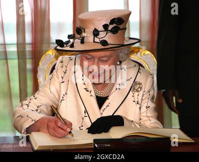 La reine Elizabeth II sourit alors qu'elle signe le livre des visiteurs à la maison d'État, Entebbe, en Ouganda.La Reine ouvrira vendredi la réunion des chefs de gouvernement du Commonwealth.Plus de 5000 délégués, le prince de Galles et la duchesse de Cornouailles, ainsi que le premier ministre britannique Gordon Brown, participeront au CHOGM. Banque D'Images