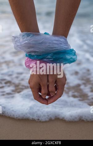 Femme mains enveloppées dans des sacs en plastique bleu, rose et blanc sur la plage. Mer sur le fond. Concept d'arrêt de la pollution plastique, sans plastique Banque D'Images