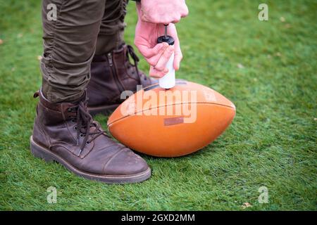 Gros plan de l'homme sur le terrain pompage d'air dans un ballon de football américain professionnel Banque D'Images