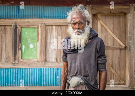 INDE, BANGLADESH - 7 DÉCEMBRE 2015 : homme ethnique senior dans des vêtements traditionnels regardant un appareil photo tout en se tenant dans la rue d'une ville âgée Banque D'Images