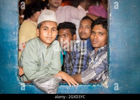 INDE, BANGLADESH - 2 DÉCEMBRE 2015 : jeune garçon ethnique sur les fenêtres de train bondées avec des hommes dans des vêtements décontractés regardant la caméra Banque D'Images