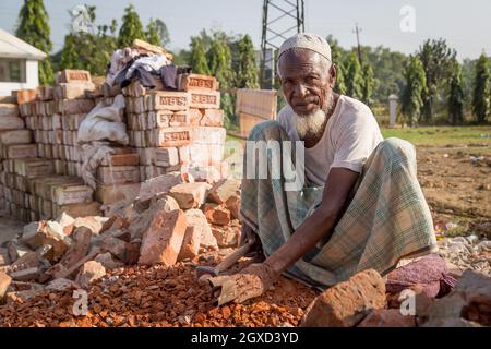 INDE, BANGLADESH - 5 DÉCEMBRE 2015 : homme ethnique en vêtements traditionnels assis sur un toit en bois, regardant la caméra tout en travaillant dans l'industrie de la brique dans le Banque D'Images