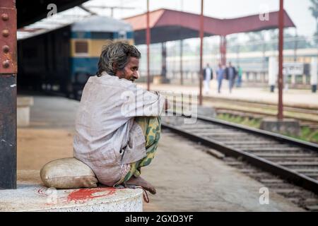 INDE, BANGLADESH - 6 DÉCEMBRE 2015 : vue latérale d'un homme ethnique dans des vêtements sales usés, assis sur une plate-forme de gare et un lookin Banque D'Images