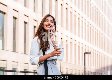 portrait horizontal d'une jeune femme indienne attrayante parlant au téléphone. Elle se trouve près des bâtiments du tribunal Banque D'Images