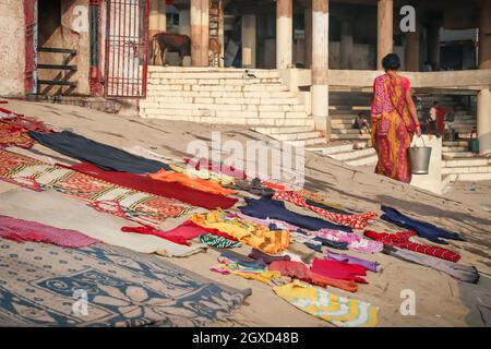 INDE, VARANASI - 27 NOVEMBRE 2015: Vue arrière de la femelle ethnique non reconnaissable dans les vêtements traditionnels marchant avec seau sur le sol et priant avec cl Banque D'Images