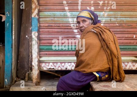 INDE, BANGLADESH - 7 DÉCEMBRE 2015 : femme ethnique âgée vêtue de vêtements traditionnels regardant un appareil-photo tout en étant assise près d'un bâtiment miteux Banque D'Images