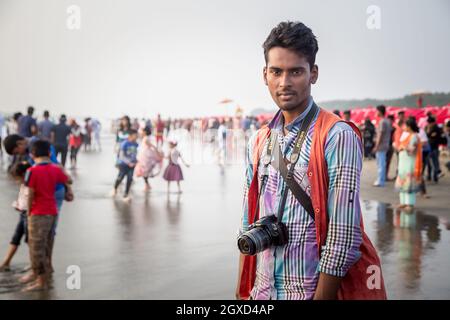 INDE, BANGLADESH - 4 DÉCEMBRE 2015 : jeune homme ethnique vêtu debout avec un appareil photo professionnel sur du sable humide sur la plage looki Banque D'Images