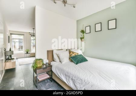 Chambre contemporaine et salle de séjour avec oreillers sur couette entre plantes en pot dans la maison avec sol carrelé Banque D'Images