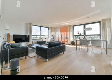 Salle à manger intérieure contemporaine avec table contre canapés et TV dans la maison avec fenêtres en journée Banque D'Images