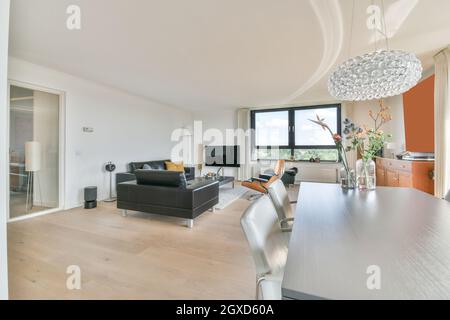 Salle à manger intérieure contemporaine avec table contre canapés et TV dans la maison avec fenêtres en journée Banque D'Images