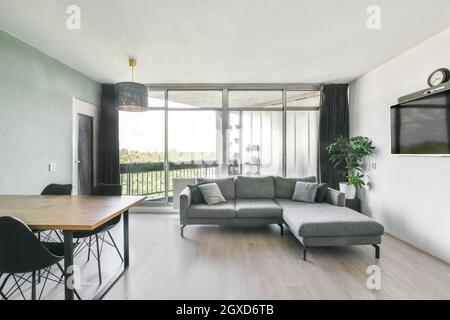 Salle à manger intérieure contemporaine avec table contre canapés et TV dans la maison avec fenêtres en journée Banque D'Images