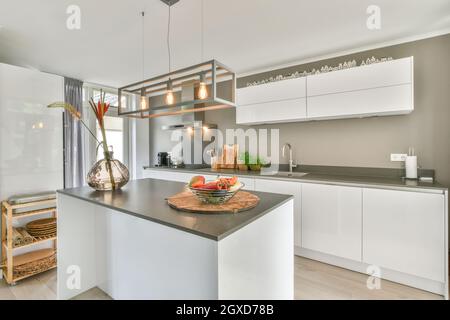 Arceaux avec fruits et légumes frais et vase avec fleurs placés sur une table dans la cuisine élégante de l'appartement contemporain Banque D'Images