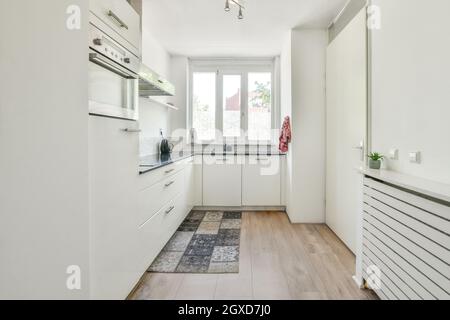Intérieur d'une cuisine élégante avec armoires blanches et moquette colorée sur parquet dans l'appartement en journée Banque D'Images