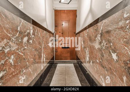 Vue panoramique de l'intérieur d'un long couloir avec murs et sol carrelés et porte en bois dans l'appartement Banque D'Images