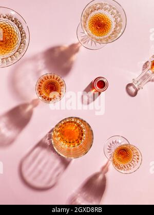 Vue de dessus des gobelets en verre remplis de whisky jetant des ombres créatives sur fond rose en studio Banque D'Images