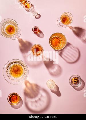 Vue de dessus des gobelets en verre remplis de whisky jetant des ombres créatives sur fond rose en studio Banque D'Images