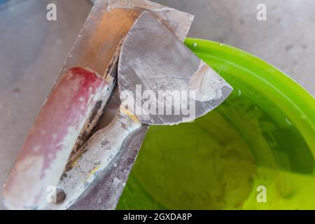 Vue de dessus des outils de construction dans le godet sur le fond en béton. Jeu d'outils à truelle et de spatule en plâtre assortis Banque D'Images