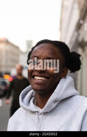 Ravi Afro-américaine androgynes femme souriant largement en se tenant dans la rue et regardant la caméra Banque D'Images