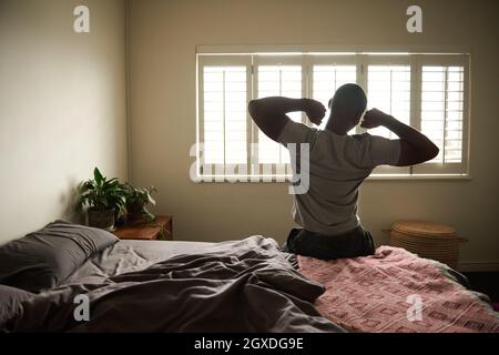 Un jeune homme africain s'étirant sur son lit le matin Banque D'Images