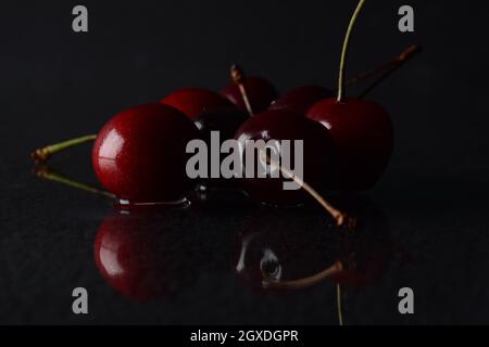 Cerises, avec des gouttes d'eau sur un fond noir avec réflexion Banque D'Images