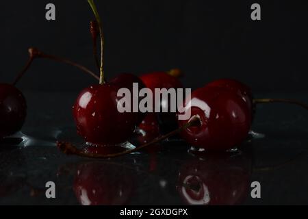 Cerises, avec des gouttes d'eau sur un fond noir avec réflexion Banque D'Images