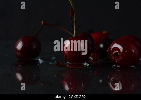 Cerises, avec des gouttes d'eau sur un fond noir avec réflexion Banque D'Images