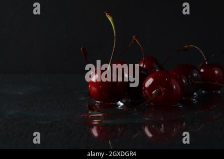Cerises, avec des gouttes d'eau sur un fond noir avec réflexion Banque D'Images