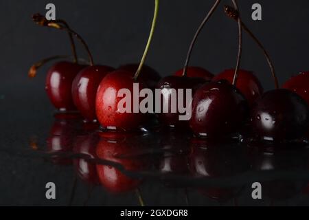 Cerises, avec des gouttes d'eau sur un fond noir avec réflexion Banque D'Images