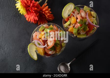 Salade de ceviche aux crevettes, aux oranges et à l'avocat dans un bol en verre sur fond gris ou foncé. Cuisine latino-américaine. Délicieux cevich aux crevettes fraîchement préparées Banque D'Images