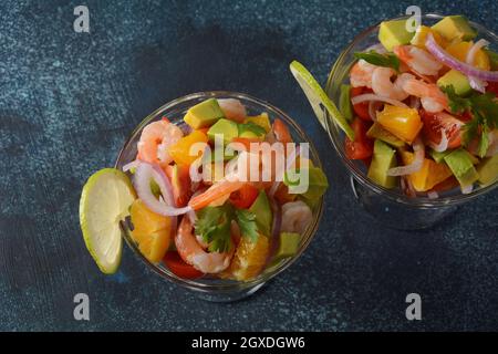 Salade de ceviche aux crevettes, aux oranges et à l'avocat dans un bol en verre sur fond gris ou foncé. Cuisine latino-américaine. Délicieux cevich aux crevettes fraîchement préparées Banque D'Images