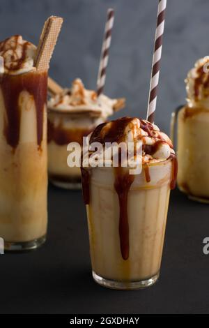 Assortiment de verres avec milkshake au caramel sucré, glace à la vanille et biscuits cachets servis sur table Banque D'Images