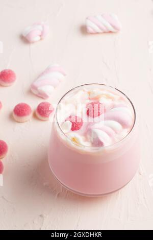 Verre de chocolat blanc chaud et doux avec bonbons roses en gelée et guimauve servi sur une table blanche Banque D'Images