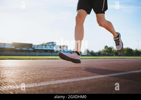 De dessous de récolte sportif en train de courir pendant l'entraînement sur piste sous ciel nuageux dans la ville ensoleillée Banque D'Images