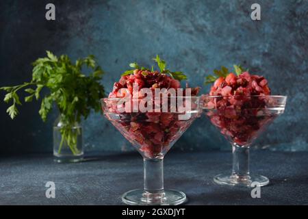 Vinegret ou vinaigrette. Salade rouge russe traditionnelle avec légumes cuits et marinés, petits pois, betteraves, dans deux bols en verre sur fond gris. Banque D'Images