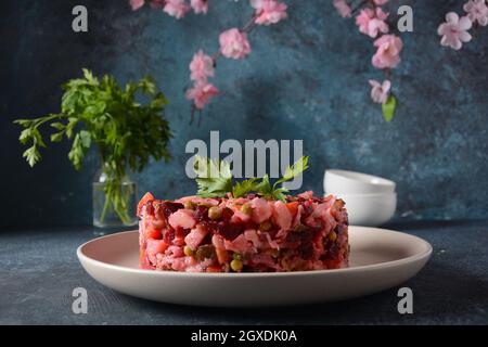 Vinegret ou vinaigrette. Salade rouge russe traditionnelle avec légumes cuits et marinés, petits pois, betteraves, en plaque blanche sur fond gris. Banque D'Images